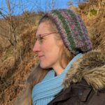 Dorothee steht auf einem Waldweg im Sonnenschein und blickt in die Ferne