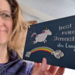 Auf dem Bild ist Dorothee zu sehen, wie sie ein Schild in der Hand hält. Darauf ist ein Einhorn auf einem Regenbogen abgebildet und daneben steht der Spruch: Fresst meinen Sternenstaub, ihr Langweiler