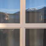 Eine Spiegelung der Alpen und von Dorothee, wie sie die Spiegelung fotografiert auf einer Balkontür