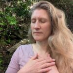 Dorothee sitzt mit geschlossenen Augen und den Händen vor dem Oberkörper in einer meditativ versunkenen Stimmung auf der Terrasse