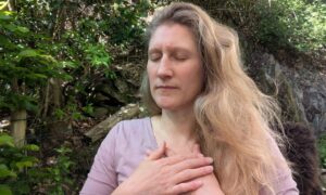Dorothee sitzt mit geschlossenen Augen und den Händen vor dem Oberkörper in einer meditativ versunkenen Stimmung auf der Terrasse