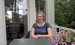 Dorothee sitzt in einem Cafe an einem Tisch mit rosafarbenen Blumen auf dem Tisch