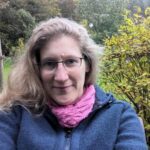 Dorothee sitzt auf einer Bank im Garten und lächelt in die Kamera