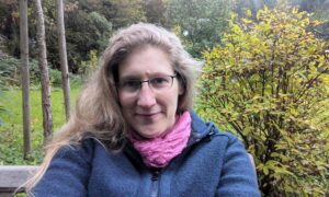 Dorothee sitzt auf einer Bank im Garten und lächelt in die Kamera