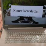 Ein Laptop auf einem Tisch, auf dem Bildschirm steht auf einem Papier Neuer Newsletter. Das Papier ist in eine Schreibmaschine eingespannt